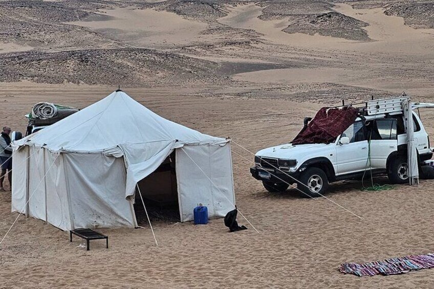 Un terrain de camping dans le désert, avec une tente, un SUV blanc et une petite table. 1