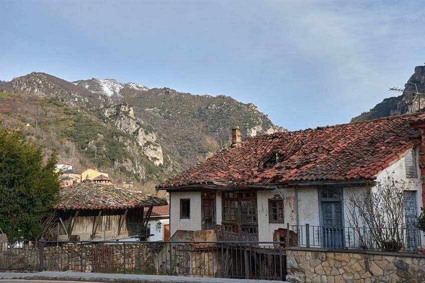 A rural village with traditional houses, a stone wall, and mountains in the background. 3