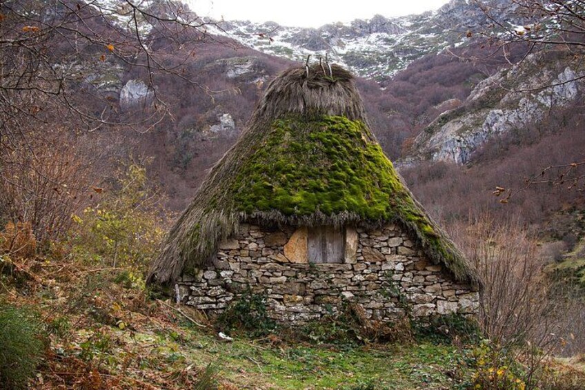 A traditional thatched-roof house with a stone base, surrounded by a mountainous landscape. 3