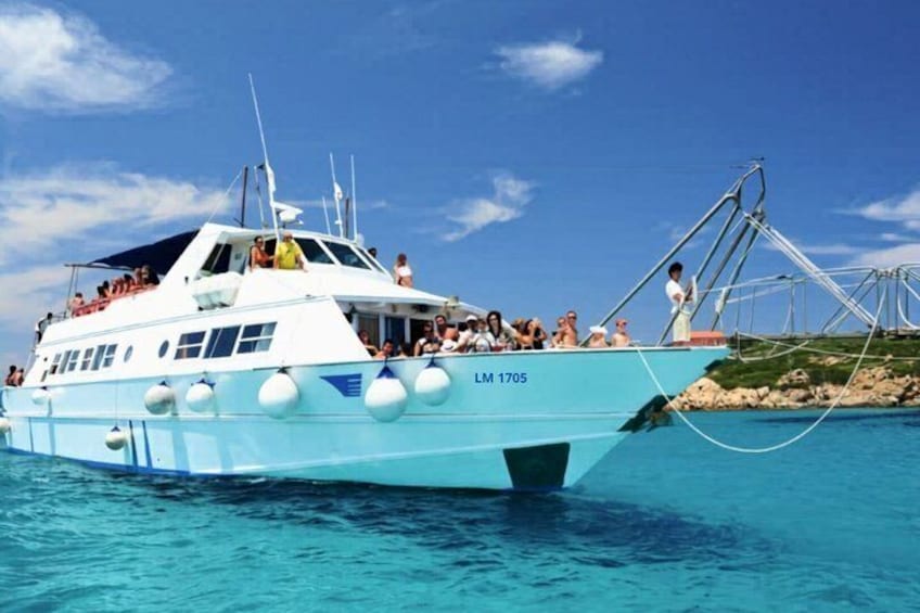 Un barco grande con gente a bordo, llamado LM 1705, atracado en un muelle con agua azul cristalina. 1