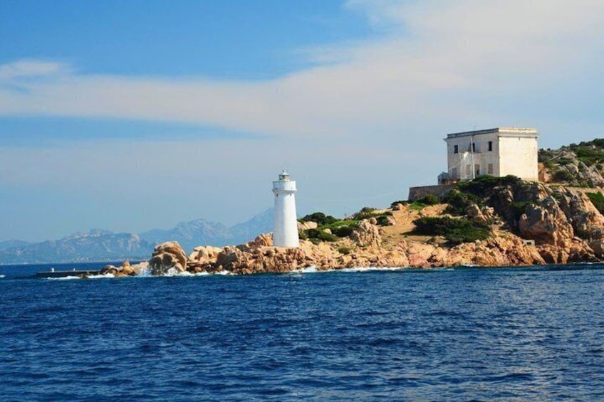 Un faro sobre un promontorio rocoso, con un edificio en una colina al fondo. 2