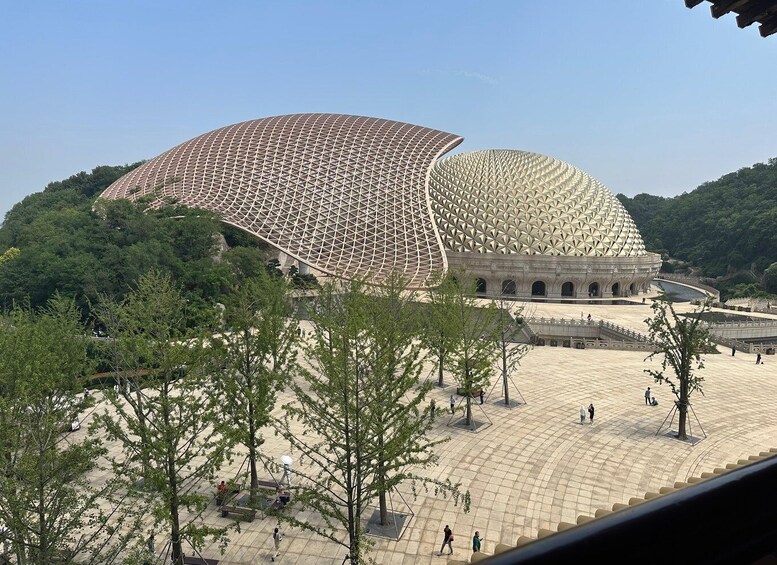 A large, dome-shaped stadium with a patterned roof, surrounded by a spacious plaza and trees. 2