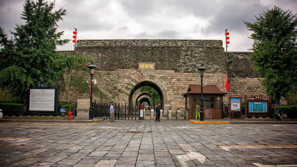A stone archway leading to a traditional building, with red lanterns on poles and a signboard on the left. 4