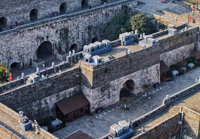 An aerial view of a historic stone fortress with multiple arched gateways, a rooftop with modern air conditioning units, and a paved courtyard. 5