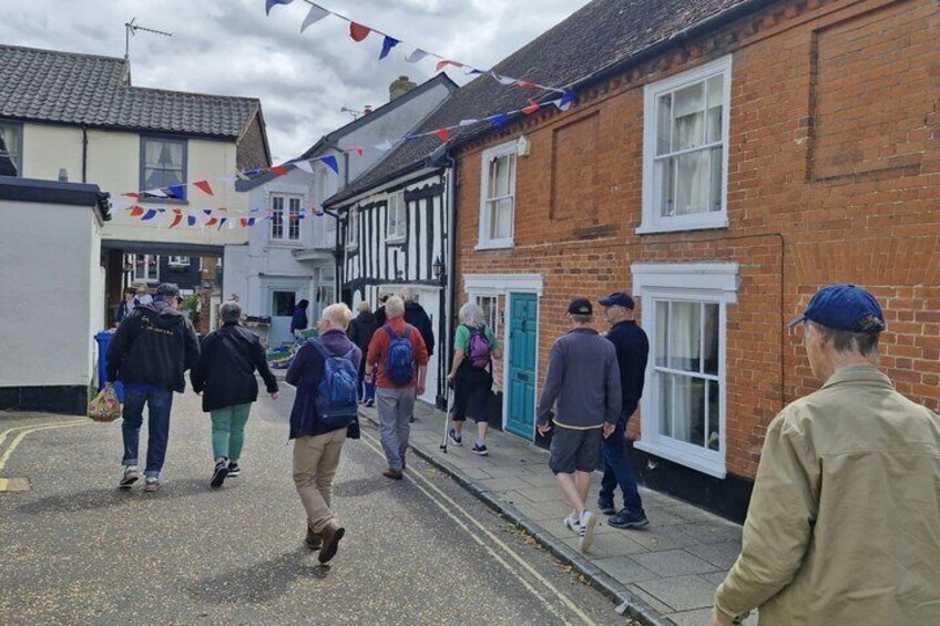 A group of people walking on a street with houses and a blue sky. 5