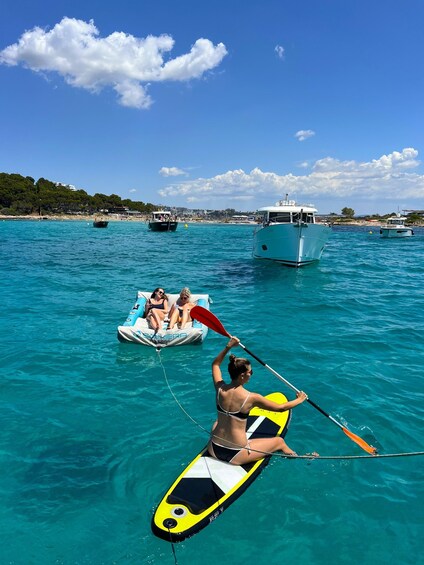 A clear blue sea with boats and a person paddling on a yellow paddleboard. 3