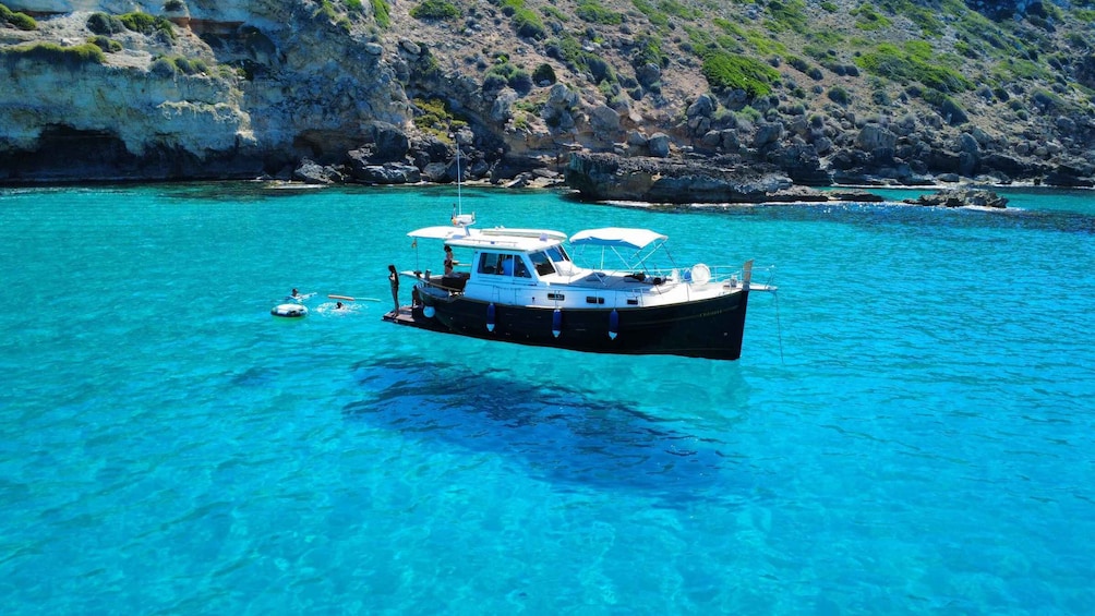 A boat anchored in clear turquoise water with rocky cliffs in the background. 1
