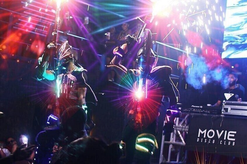 A live music performance with a DJ and a band on stage, surrounded by a crowd. 1