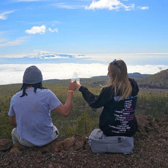 Two people sitting on a rocky outcrop overlooking a mountainous landscape with a clear sky. 5