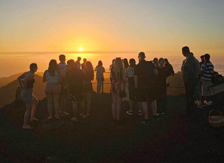 A group of people standing on a hill overlooking a sunset over the ocean. 2