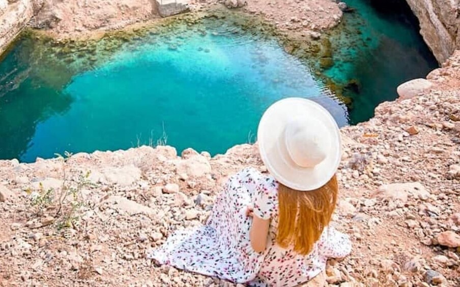A person sitting on a rocky outcrop overlooking a turquoise pool. 1