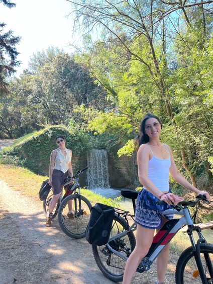 Two people with bicycles near a waterfall in a wooded area. 5