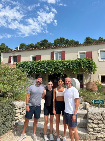 A group of people standing in front of a building with red shutters and a stone wall. 2