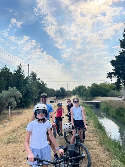 A group of people on bicycles along a canal path with trees and a bridge in the background. 4