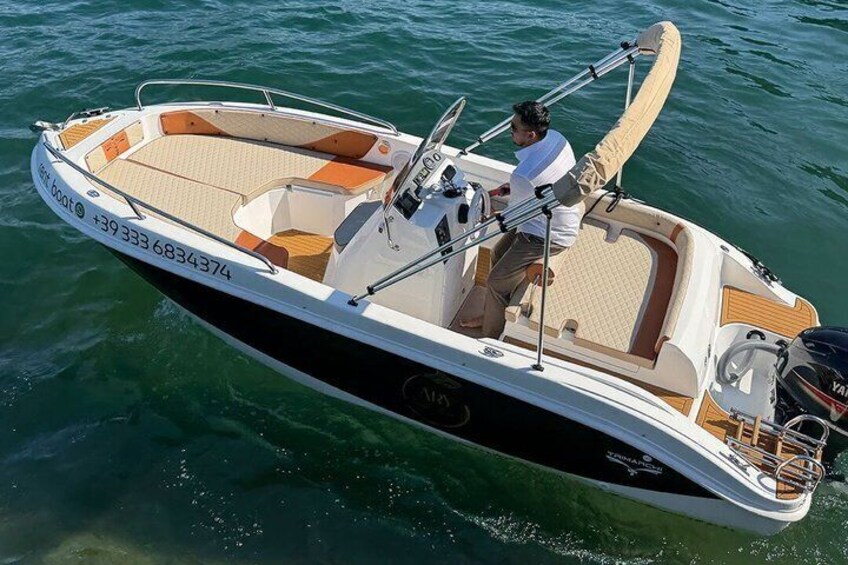 Un bateau à moteur aux couleurs beige et blanc, avec une personne aux commandes et une vague qui se forme derrière lui. 1