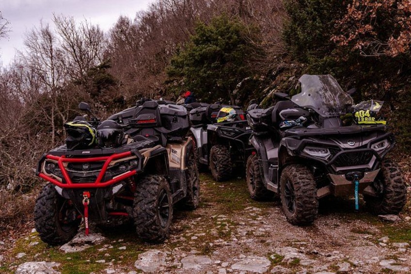 Four all-terrain vehicles parked on a rocky path surrounded by trees. 2
