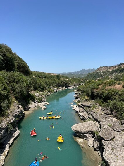 A river with kayaks and a red boat, surrounded by rocky terrain and greenery. 2