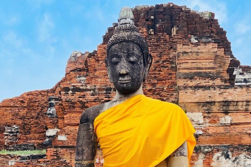 A large Buddha statue in a yellow robe with a brick temple structure in the background. 2