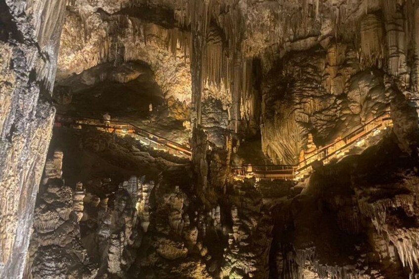 A cave with stalactites and stalagmites, illuminated by artificial lighting, and a wooden walkway. 5
