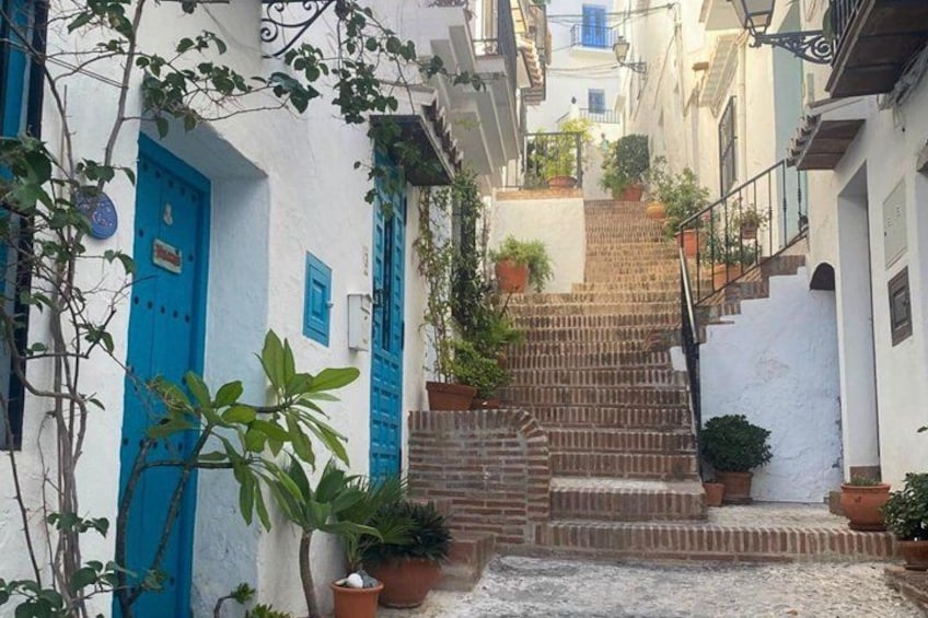 A narrow street with a staircase leading up to a building, surrounded by white walls and blue doors. 2