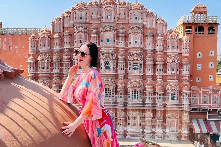 A person in a colorful dress standing in front of a large, ornate building with multiple domes and intricate designs. 1