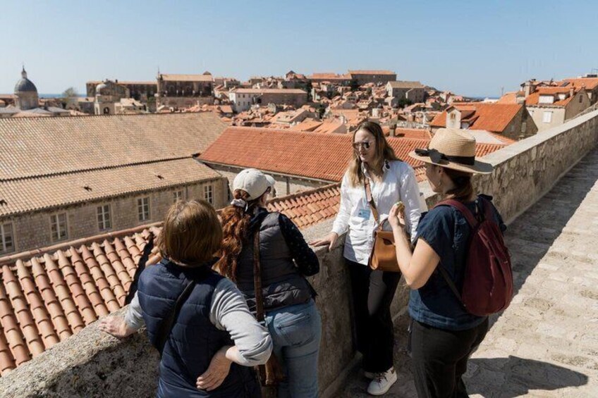 Turisti su un tetto con vista su un paesaggio urbano caratterizzato da tetti in terracotta ed edifici storici. 3