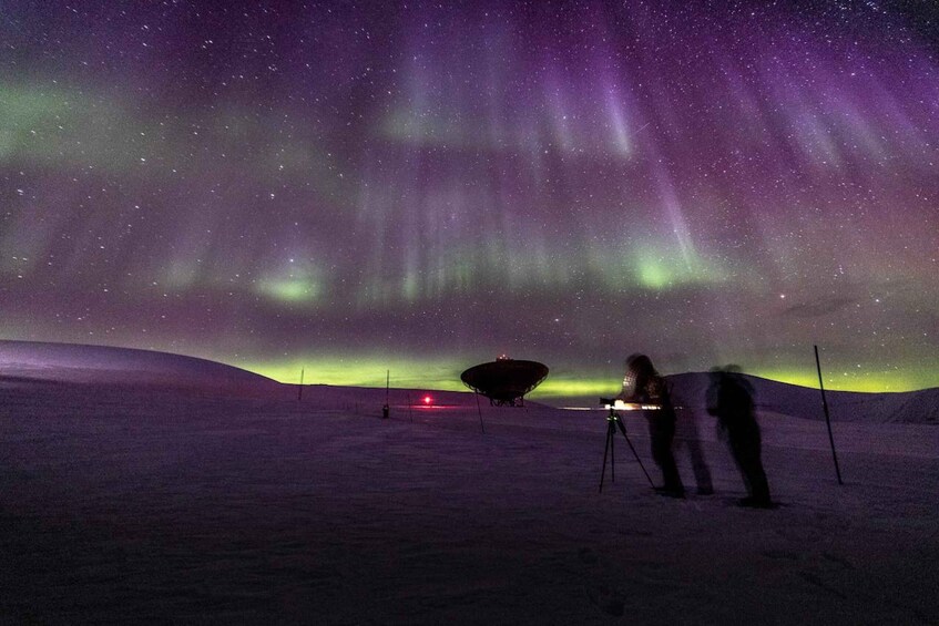 A snowy landscape with the Northern Lights and a large satellite dish. 2
