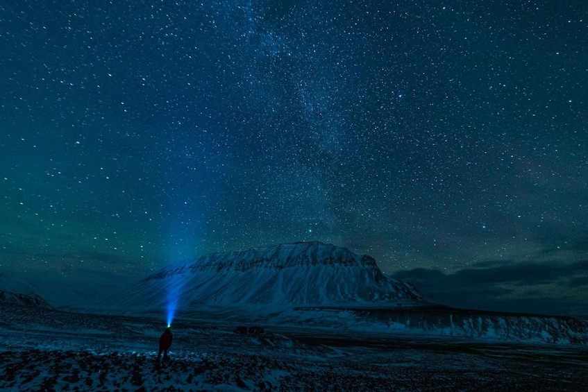 A person standing on a snowy landscape under a starry night sky with a mountain in the background. 3