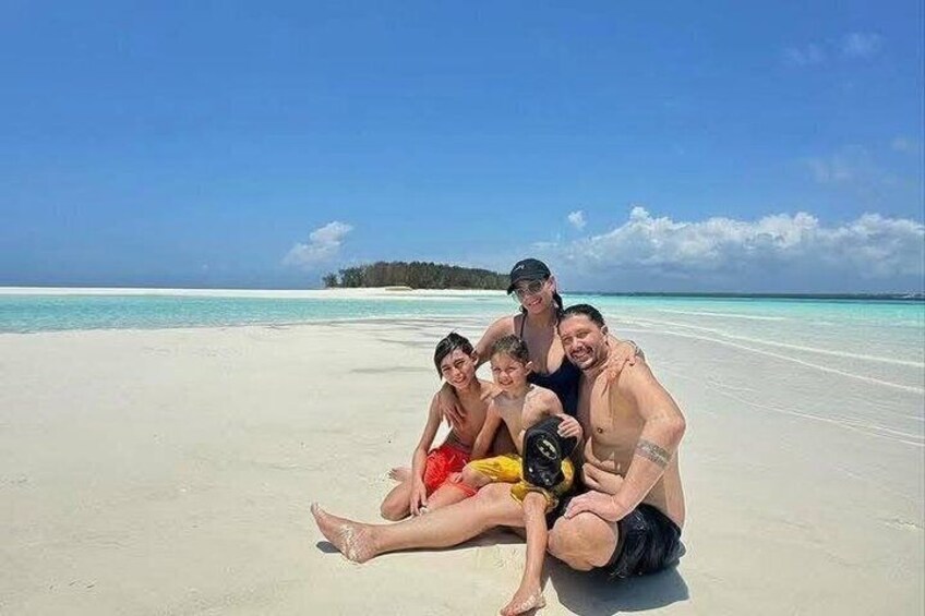 En familj på en sandstrand med kristallklart, turkosfärgat vatten och en ö i fjärran. 1