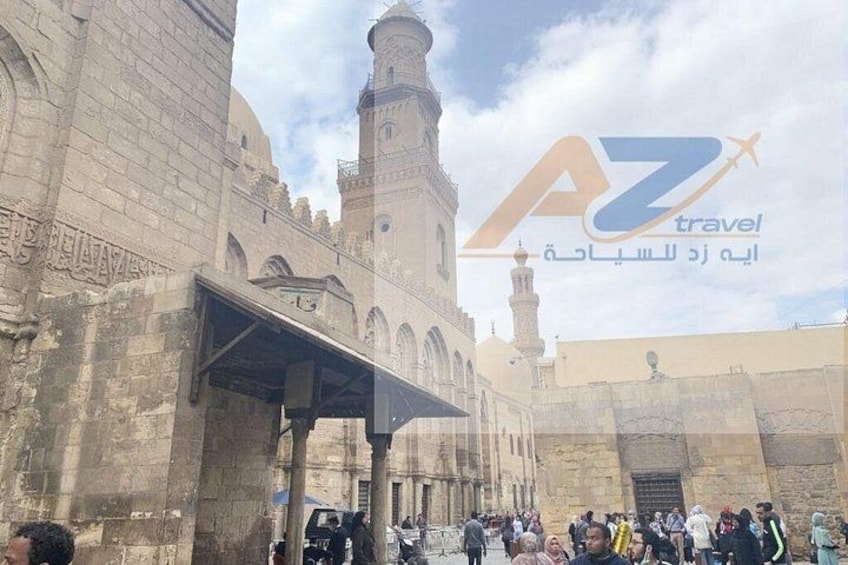 A historic building with arches and a minaret, surrounded by a crowd. 5