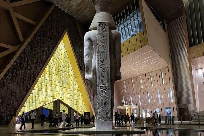 Un espacio interior amplio con una escultura destacada, una estructura piramidal amarilla y un moderno frente de edificio. 4