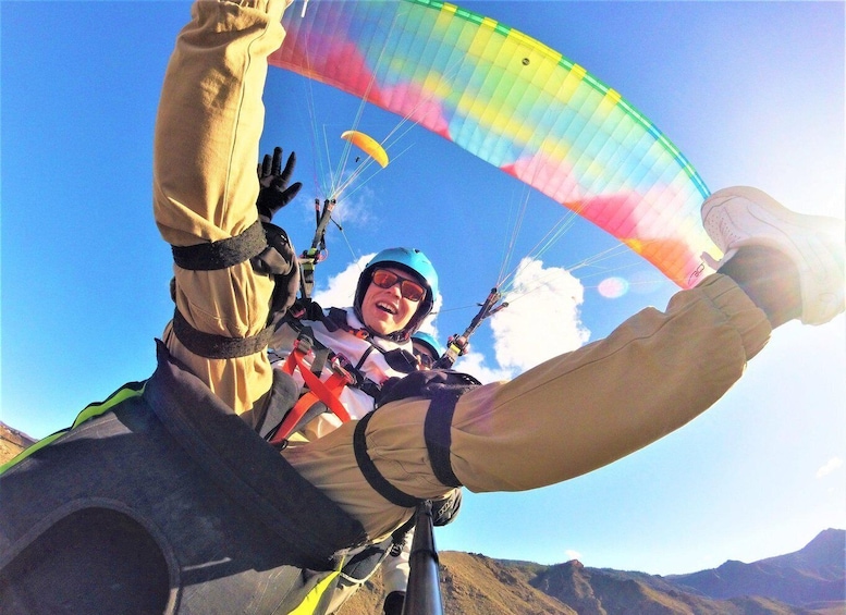 A person paragliding with a colorful canopy, wearing a helmet and harness, against a clear sky. 2