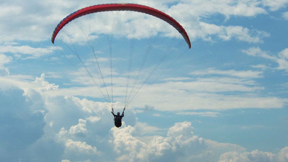 A person paragliding with a red canopy above a cloudy sky. 5