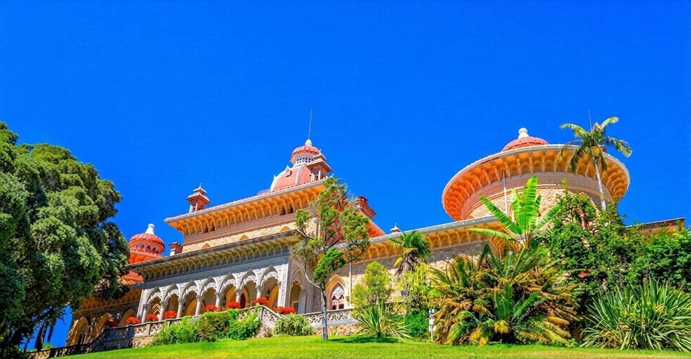 A large, ornate building with domed roofs and a circular structure, surrounded by lush greenery. 4