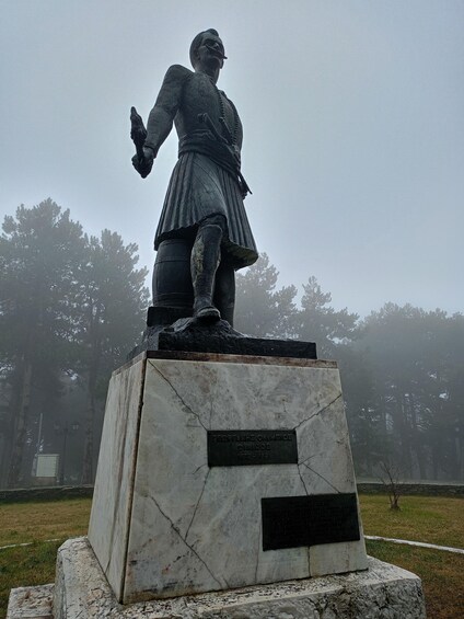 A statue of a historical figure on a pedestal with inscriptions, surrounded by trees and fog. 4
