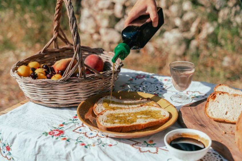 Una mesa al aire libre con una cesta de frutas, una tostada con mantequilla, una taza de café y un vaso de agua. 1
