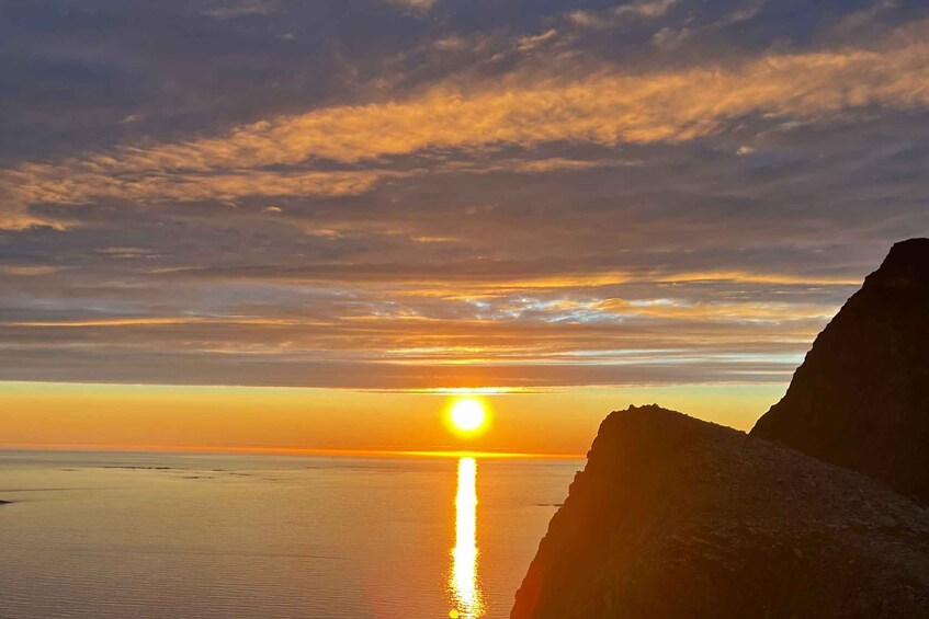 A sunset over a calm sea with a rocky coastline. 1