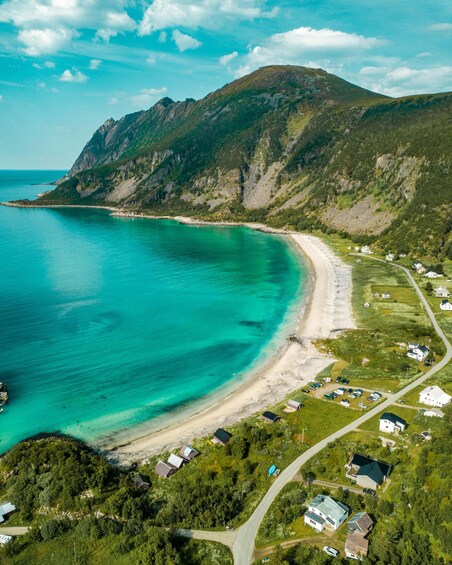 A coastal landscape with turquoise waters, a sandy beach, and a cluster of houses. 2