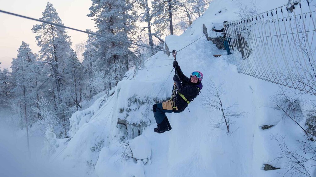 A person engaged in a winter sport, suspended by a harness, in a snowy forest with trees and a fence. 2