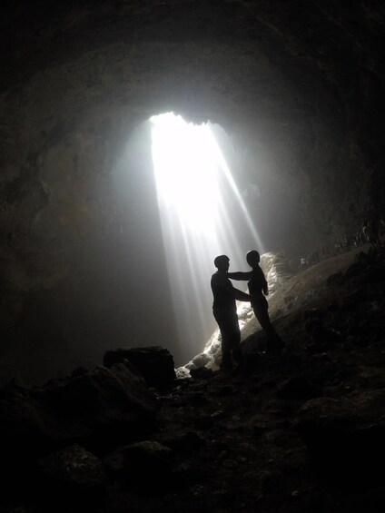 Two people standing in a cave with a bright light shining through the entrance. 1