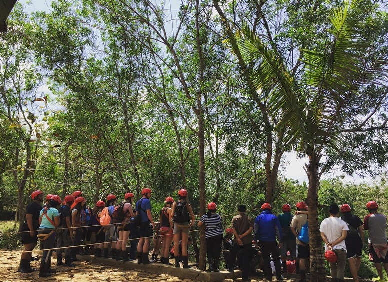 A group of people with helmets standing on a rope bridge in a forested area. 4