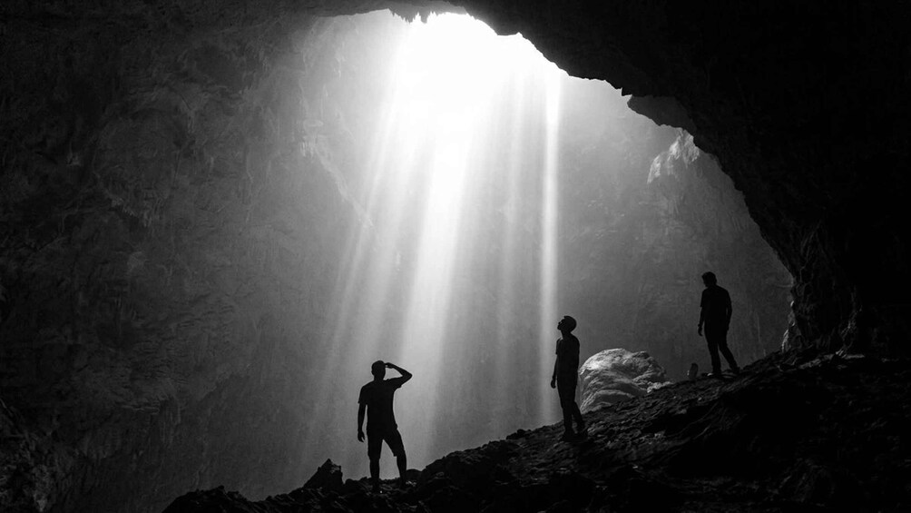 A cave with a large opening, sunlight streaming through, and silhouettes of people inside. 2