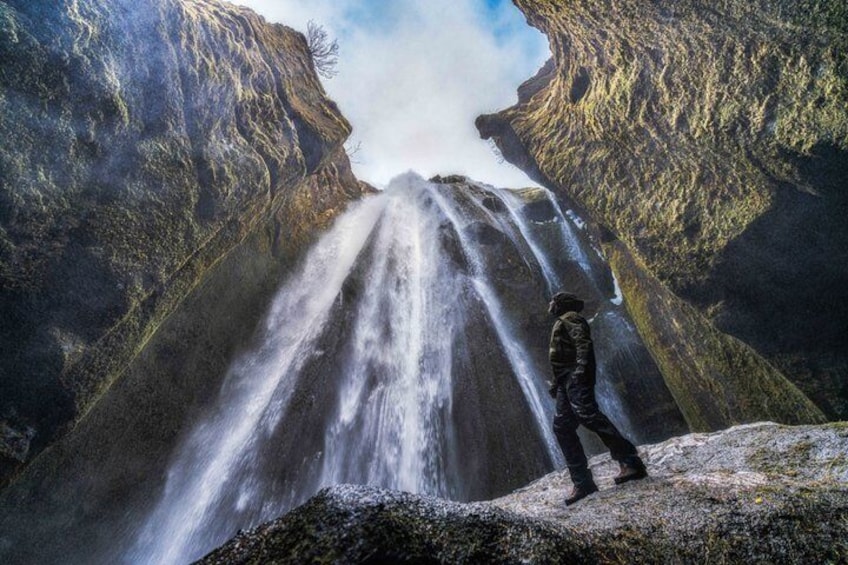 A person standing on a rocky outcrop overlooking a waterfall. 1