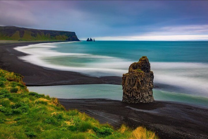 A coastal landscape with a prominent rock formation, a sandy beach, and a distant cliff. 3