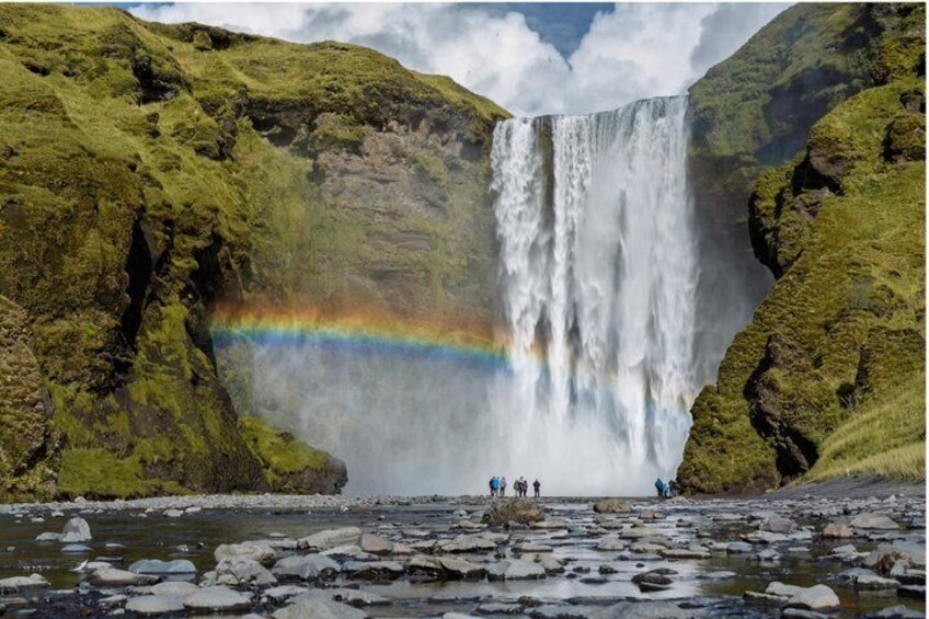A waterfall with a rainbow, surrounded by green mossy rocks. 2