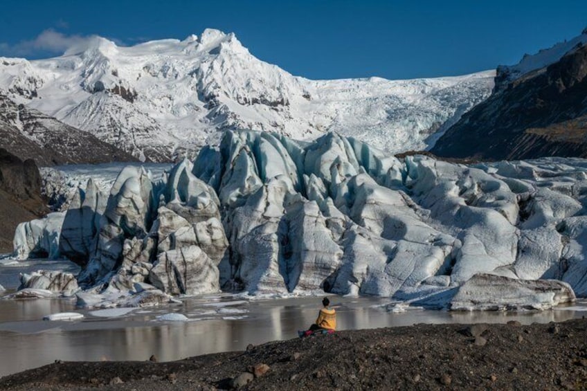 A glacier with a person in a yellow jacket sitting on the ground. 4