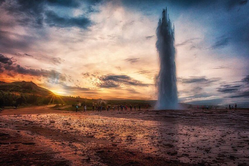 A geyser with people observing it, set against a sunset sky. 3