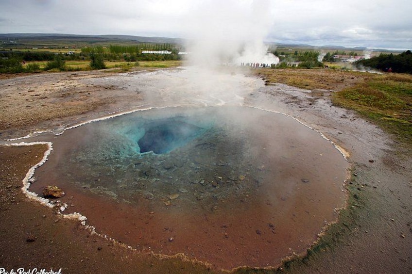 A geothermal hot spring with steam rising, surrounded by a barren landscape. 2