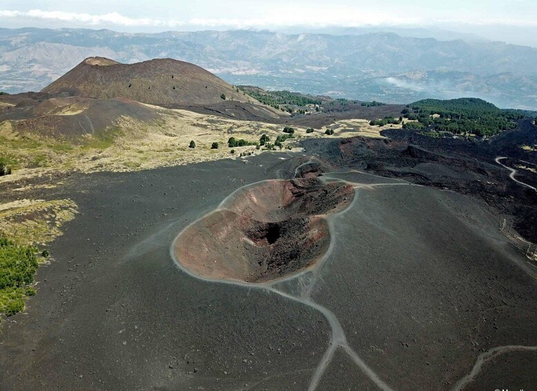 A volcanic crater with a road leading to it, surrounded by hills and sparse vegetation. 1