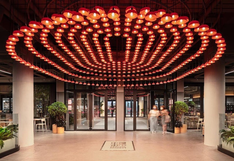 A modern building entrance with a circular arrangement of hanging lights and potted plants. 5